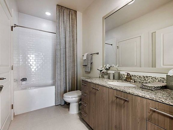 Bath with granite countertops, brown cabinetry, hard surface flooring and tiled bathtub
