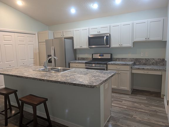 Large kitchen island, dishwasher, stove, refrigerator & microwave in stainless steel. Desk area.