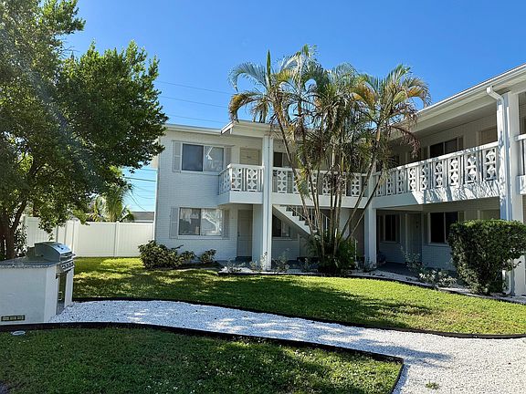 Charming white apartment building with lush greenery and inviting balcony, perfect for enjoying sunny days.