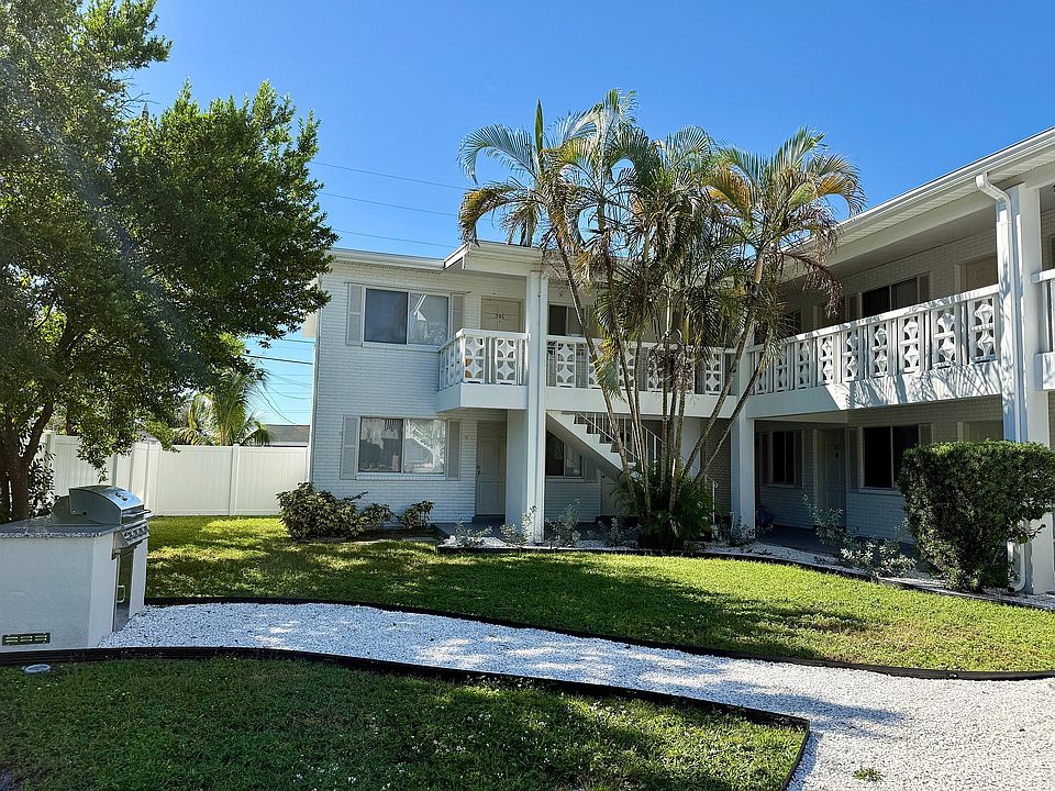 Charming white apartment building with lush greenery and inviting balcony, perfect for enjoying sunny days.