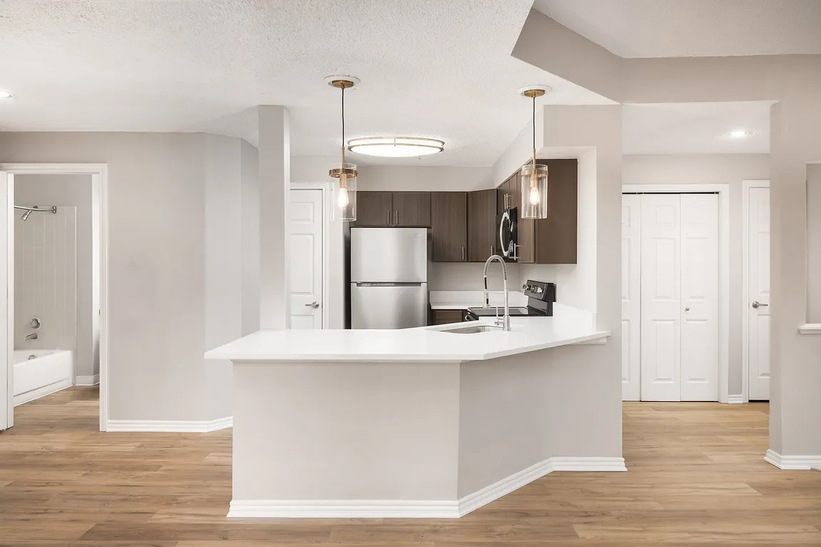 Modern apartment kitchen with elegant white countertops, stainless steel appliances, and warm wood flooring.
