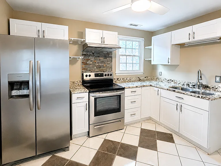 Bright, updated kitchen with granite countertops, stainless steel appliances, white cabinetry, tile flooring, and access to a private balcony. Clean, functional, and full of natural light.