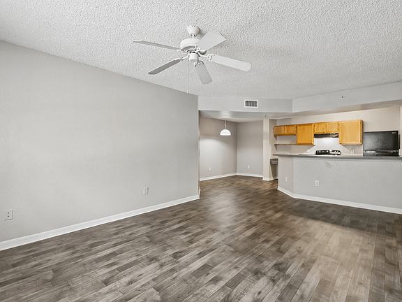 Spacious open-concept living room with wood-style flooring, breakfast bar, ceiling fan, and kitchen in a 3-bedroom, 2-bath apartment at Gregory Cove in Jacksonville, FL.