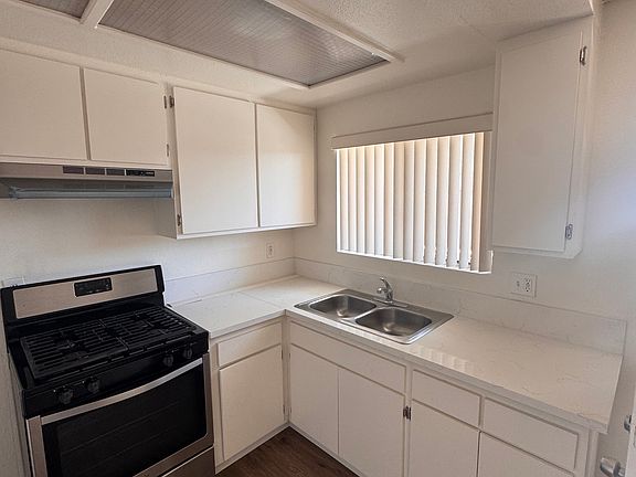 Kitchen with gas stove, white cabinets, double sink, and updated countertops.