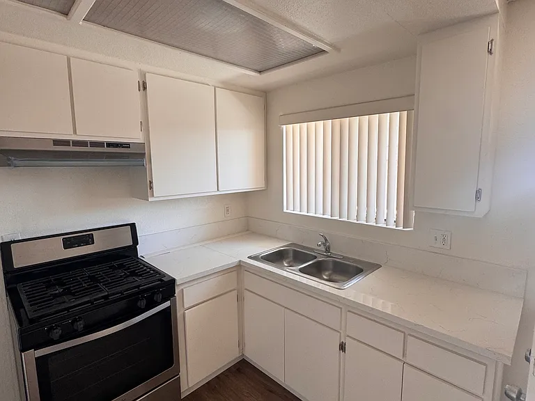 Kitchen with gas stove, white cabinets, double sink, and updated countertops.
