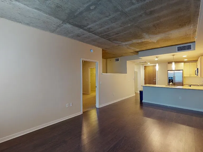 Apartment kitchen with stainless steel appliances, dining and living room with wood-style flooring.