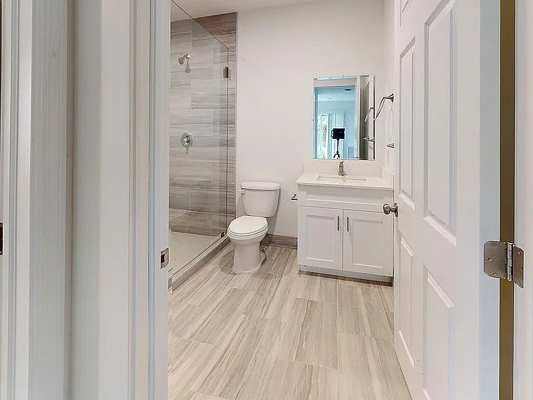Elegant modern bathroom with sleek glass shower, pristine white fixtures, and stylish wood flooring.