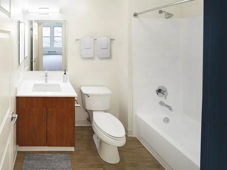 Renovated Package I bath with white quartz countertops, oak cabinetry, and hard surface flooring