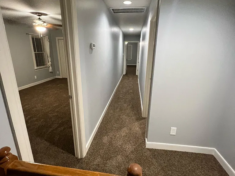 Photo from top of the stairwell looking left down the hallway. Bedroom 1 on the first left (with attic access), bedroom 2 on the right, and bedroom 3 straight ahead at the end of the hallway (bedroom above garage)