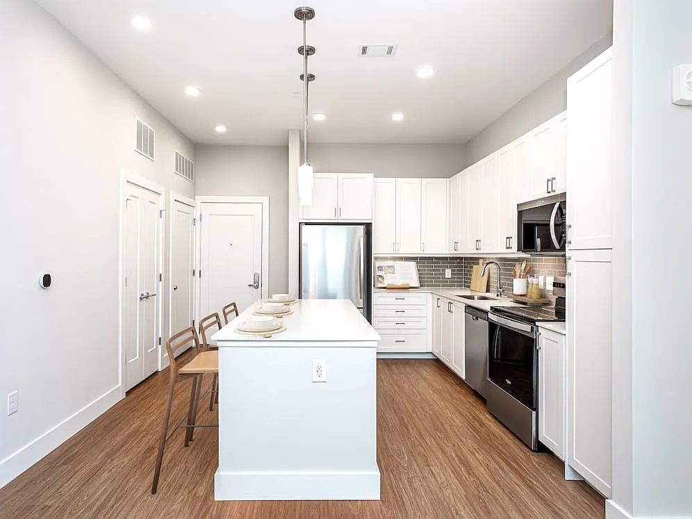 Modern kitchen with white cabinetry, undercabinet lighting, grey tile backsplash, and white quartz countertops - Avalon Carmel Commons