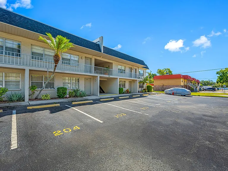 Bright and welcoming apartment complex with lush landscaping and ample parking under a clear blue sky.