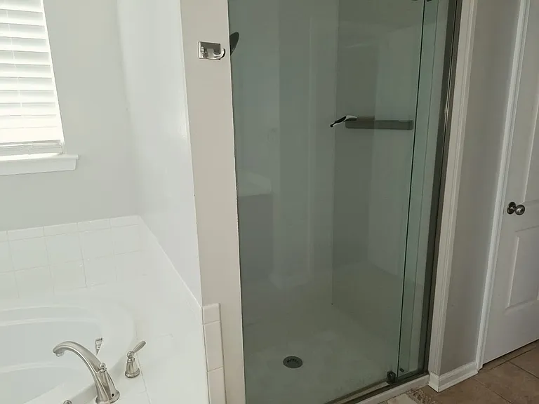 The spacious bathroom includes a walk-in glass shower, modern fixtures, and a clean, comfortable design for everyday convenience.