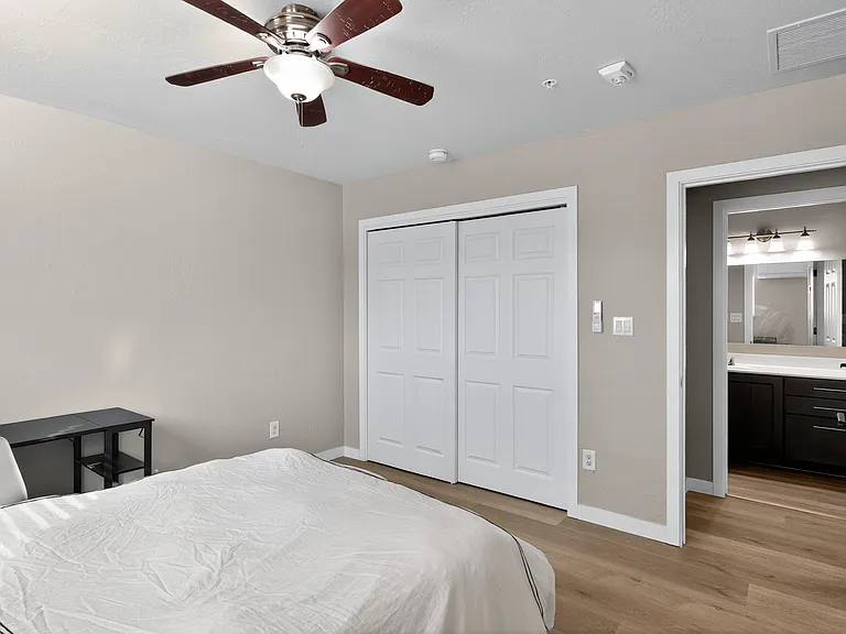 Bedroom with ceiling fan, wide sliding-door closet, and easy access to a private vanity area with ample counter space.