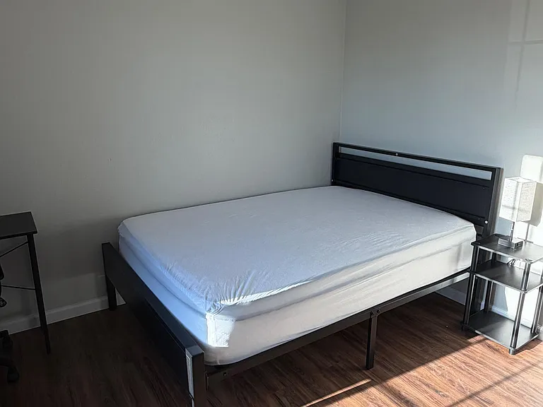 Furnished bedroom with a full bed, nightstand, and ceiling fan, plus hardwood-style flooring and natural light.