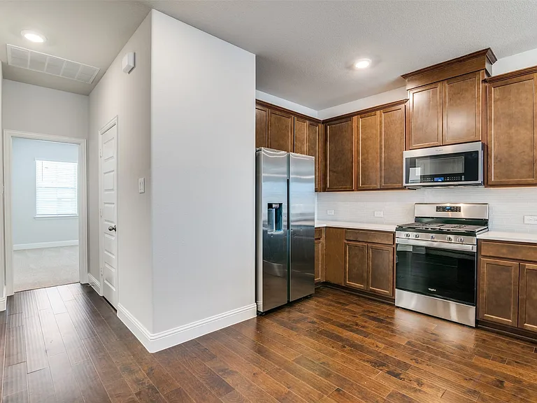 Modern kitchen featuring wood-finish flooring, stainless steel appliances, extensive cabinetry, light countertops, and a white subway tile backsplash