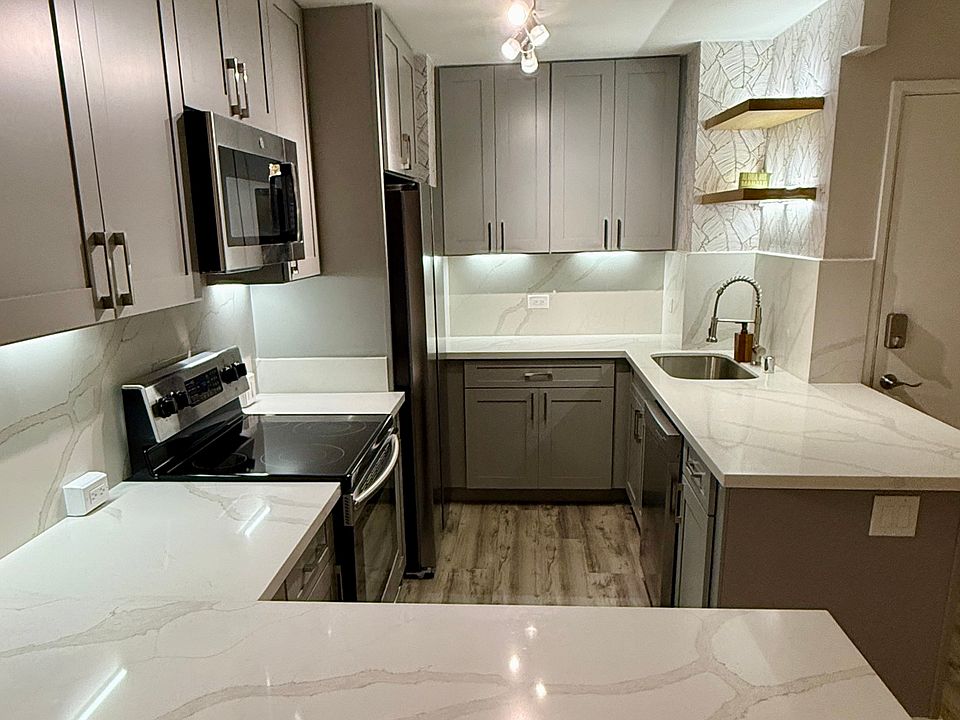 Showcasing a stunning quartz countertop throughout, seamlessly extending into a full-height backsplash for a clean, modern look. Thoughtful under-cabinet and accent uplighting brighten the space.