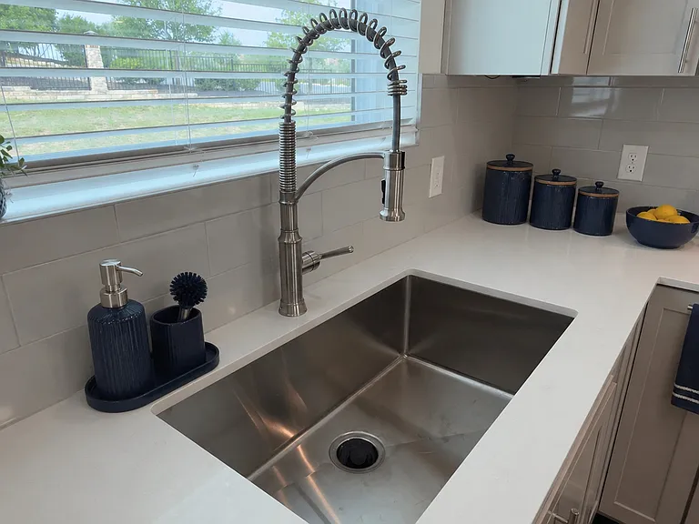 Large, deep stainless steel sink with abundant counter space, perfectly positioned beneath a window overlooking lush hillside views.