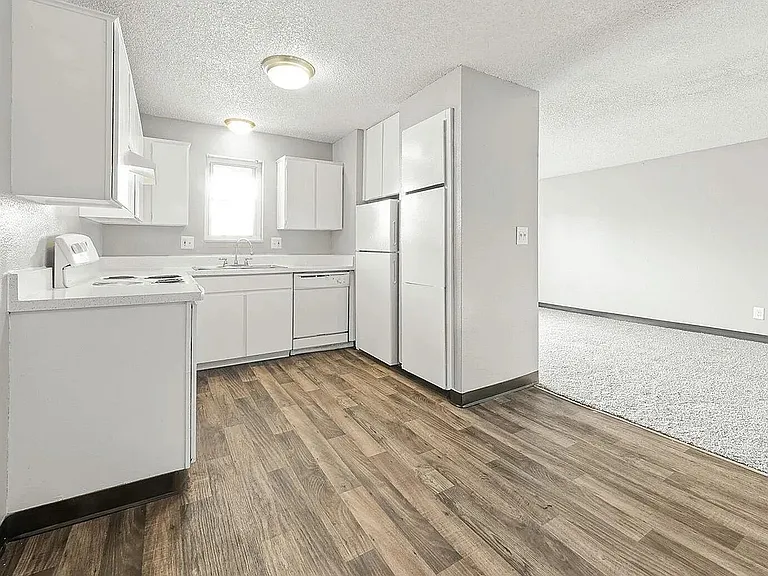 Chic and bright kitchen with sleek white cabinets, modern appliances, and inviting wood flooring leading to a spacious living area.
