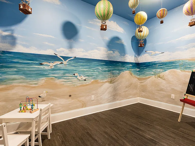 Charming kids center with a vibrant beach mural featuring seagulls and dunes, conveniently attached to the fitness center