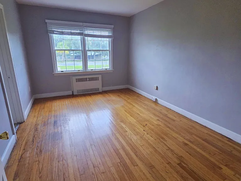 Spacious bedroom with large window and warm hardwood flooring.