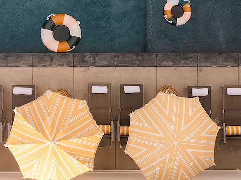 Resort-style outdoor space with a heated pool, hot tub, sun loungers with umbrellas, and cozy seating. Perfect for relaxing, sunbathing, or enjoying poolside drinks, this stylish area offers a luxurious retreat for ultimate leisure.