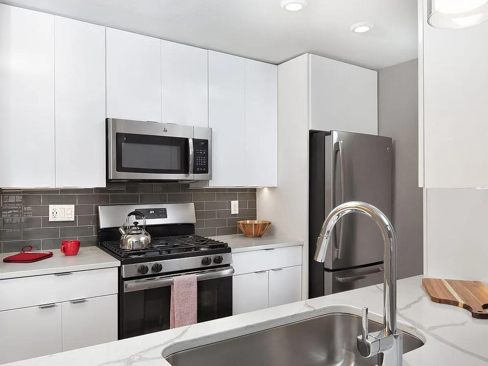 Premier Scheme kitchen with flat white cabinetry, white marbled quartz countertops, grey subway tile backsplash, stainless steel appliances, and hard surface flooring - Avalon Melville