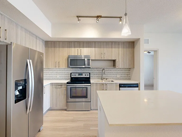 Apartment kitchen with stainless steel appliances, light counters, and wood style floor.