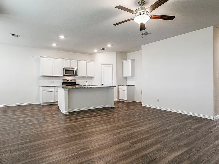 Kitchen featuring dark hardwood / wood-style floors, an island with sink, white cabinets, light stone counters, and stainless steel appliances