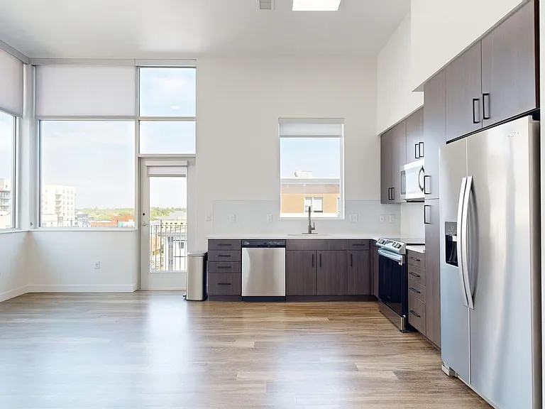 Apartment kitchen with stainless steel appliances, dining and living room with wood-style flooring.