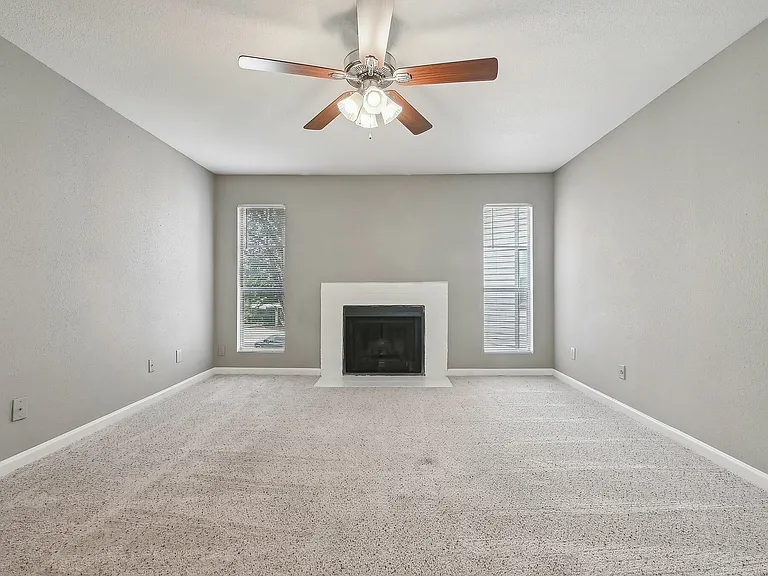 Cozy living room with plush carpet, elegant ceiling fan, and a classic fireplace, offering a serene ambiance at Driscoll Place.