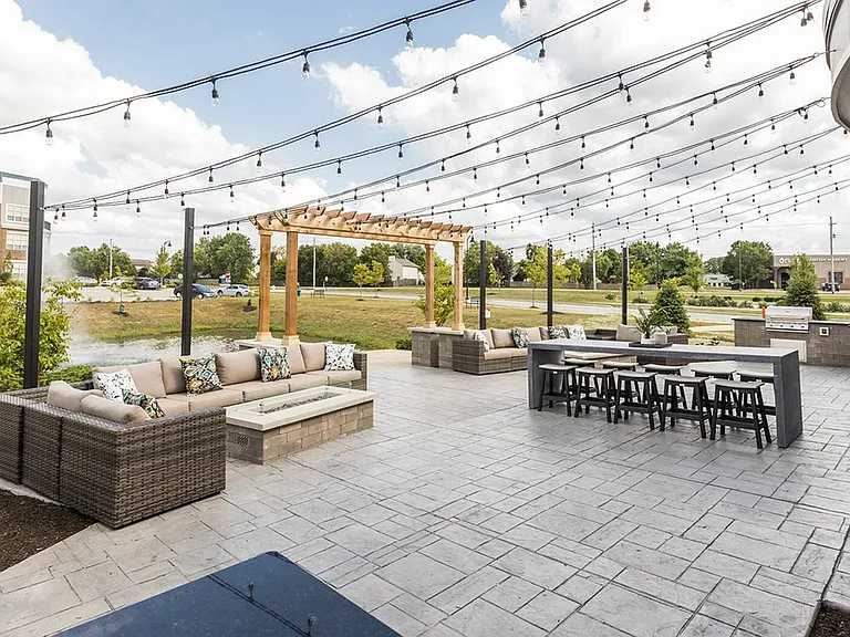 Charming outdoor patio with elegant string lights, cozy wicker seating, and a modern barbecue area overlooking serene green spaces.