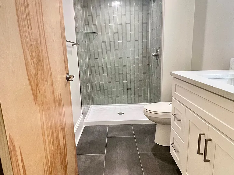 Hall bath with large format porcelain tile floor, vertical subway tile in the shower.