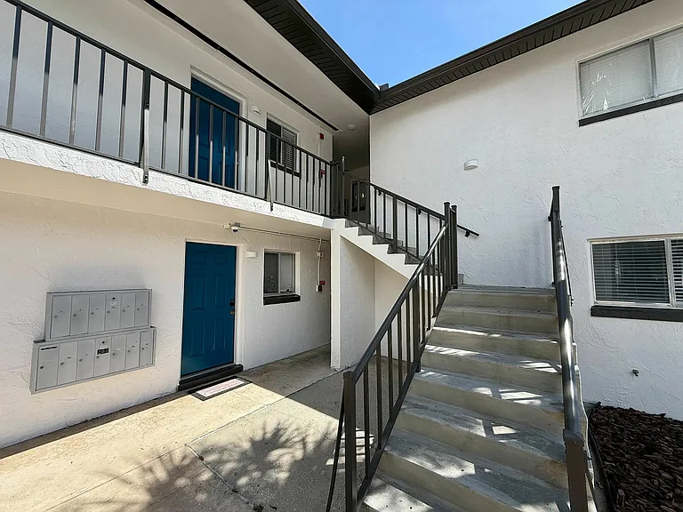 Inviting apartment entrance with modern design, featuring a vibrant blue door, accessible stairway, and stylish railings.