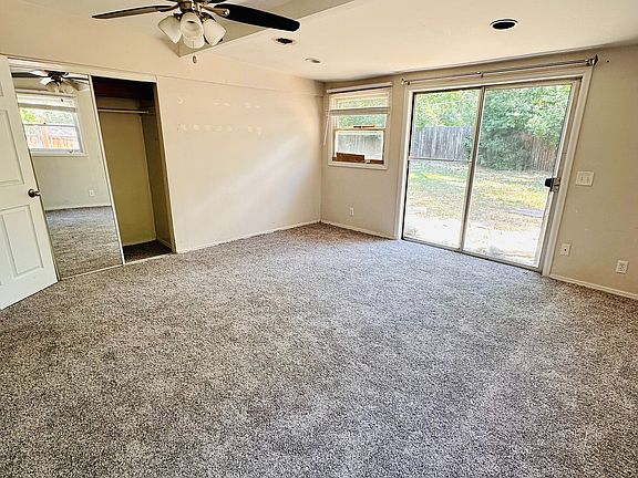 Spacious bedroom with plush carpeting, modern ceiling fan, and abundant natural light through a sliding glass door leading to a serene backyard.