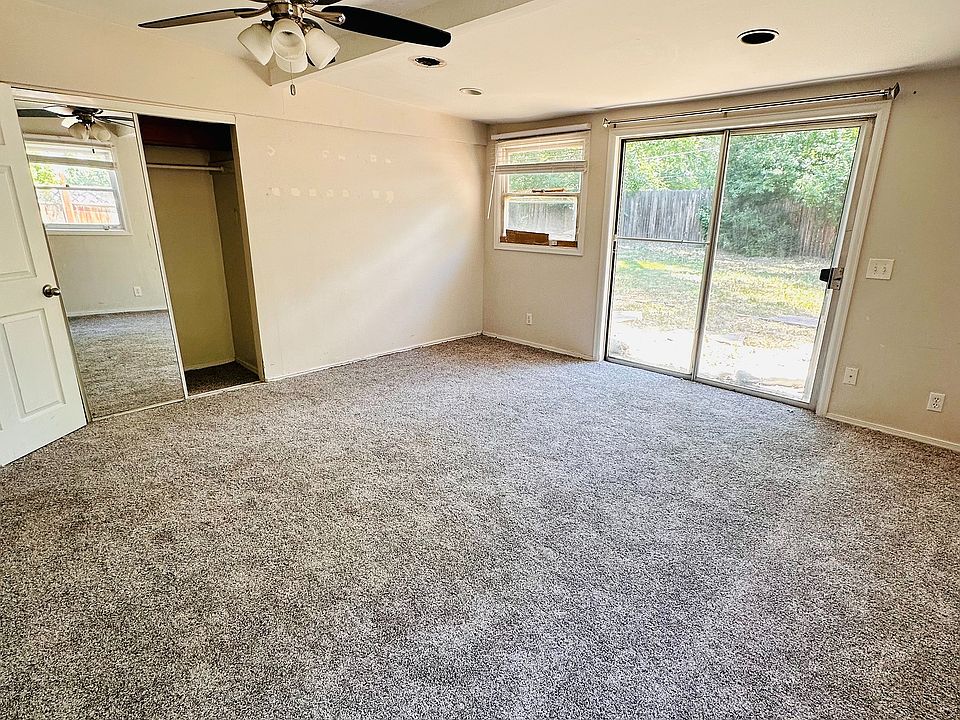 Spacious bedroom with plush carpeting, modern ceiling fan, and abundant natural light through a sliding glass door leading to a serene backyard.