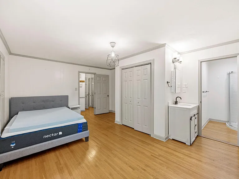 Spacious bedroom with hardwood floors, double-door closet, and an en-suite vanity with adjacent shower area.