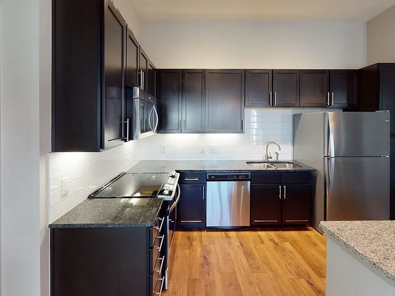 Apartment kitchen with stainless steel appliances, granite countertops and wood-style flooring.