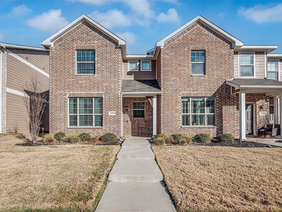Two-story brick facade townhome featuring a covered front porch, white window frames, and a concrete walkway