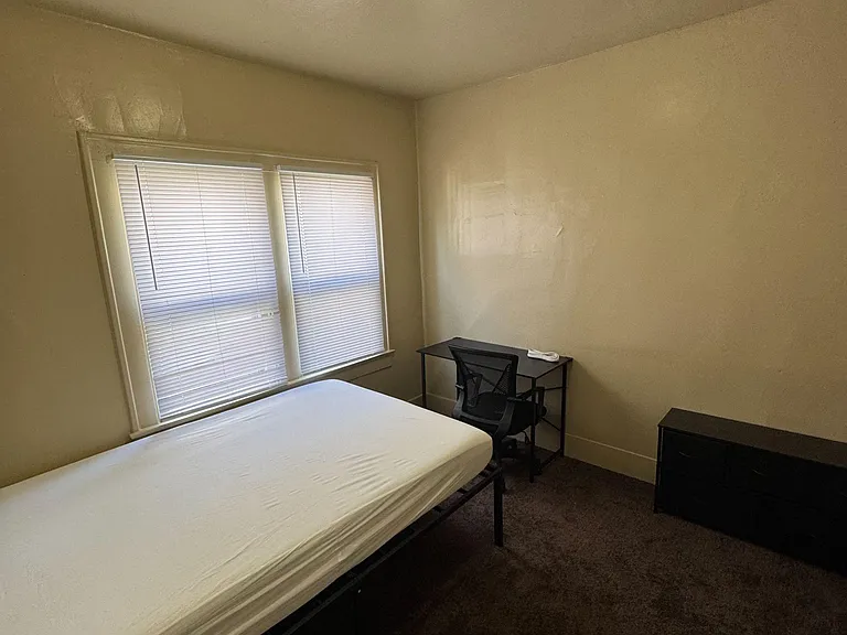 Private bedroom with a large window, overhead lighting, and space for a bed plus a work desk and storage.