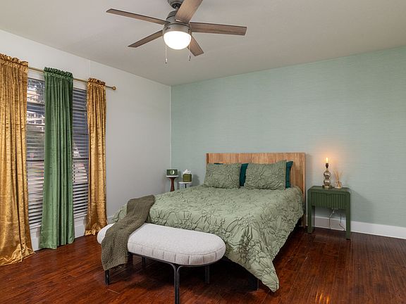 Rest in a calming bedroom with soft green tones, warm lighting, and a cozy bench at the foot of the bed. Enjoy a large TV, stylish dresser, and easy access to a spacious walk-in closet for a relaxing, comfortable stay.