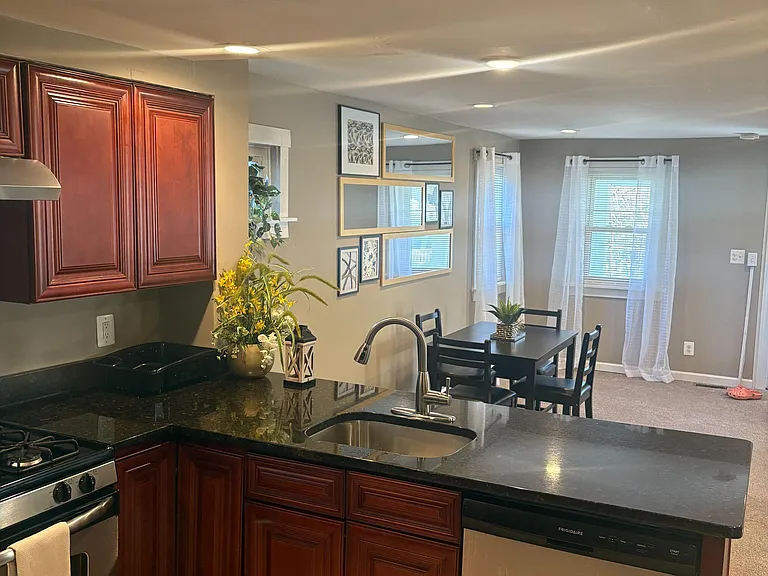 Kitchen with dark countertops, stainless appliances, and a peninsula sink opening to an adjacent dining area.