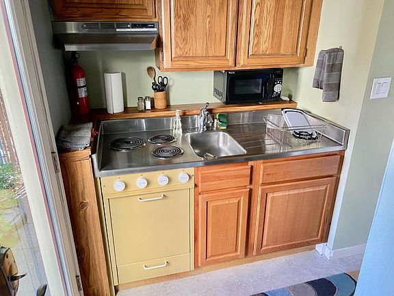 Entry door is to the left. Kitchenette has stove, oven, microwave and exhaust fan. The pantry and fridge are on the opposite wall.