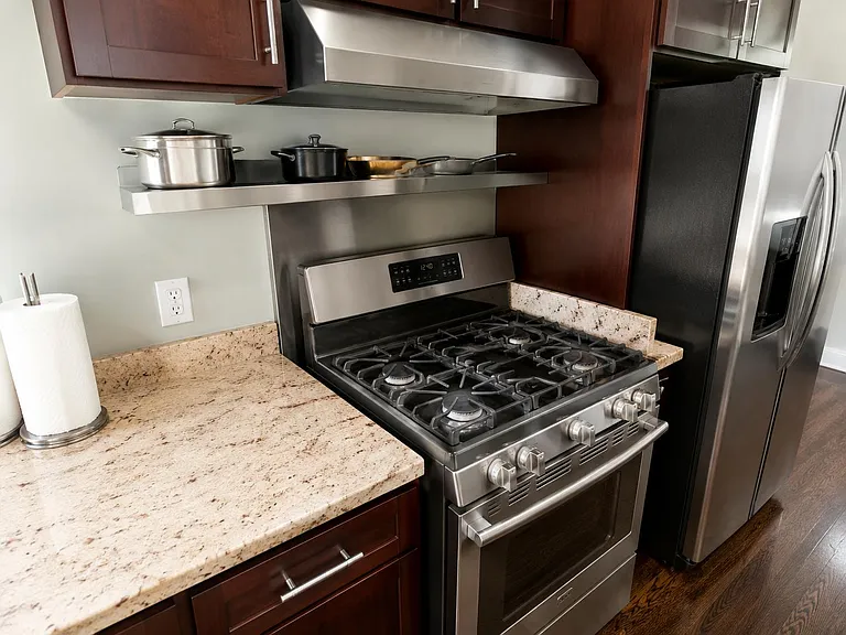 Well-equipped kitchen with a gas range, stainless steel refrigerator, vent hood, and granite counters for easy meal prep.