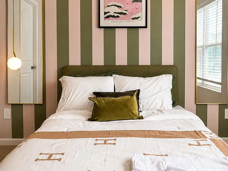 Furnished bedroom with a full bed, stylish accent wall, paired mirrors, and window blinds for easy light control.