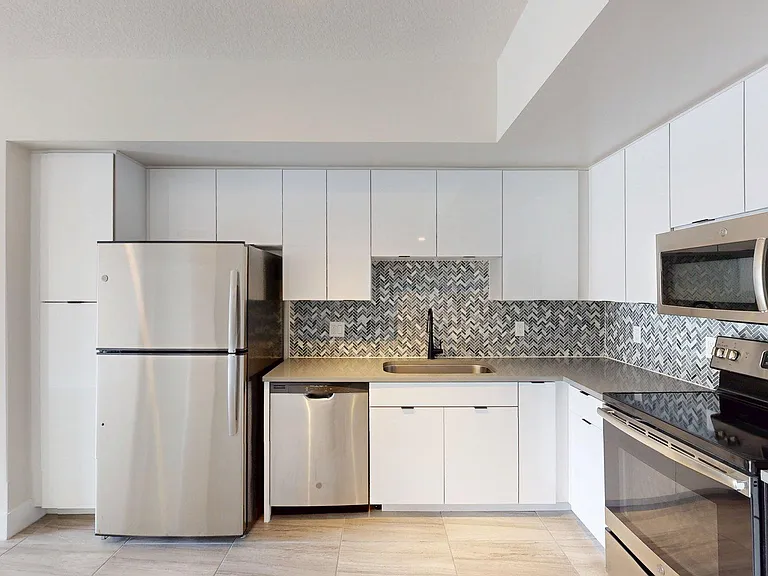 Apartment kitchen with stainless steel appliances, gray counters, and wood style floor.