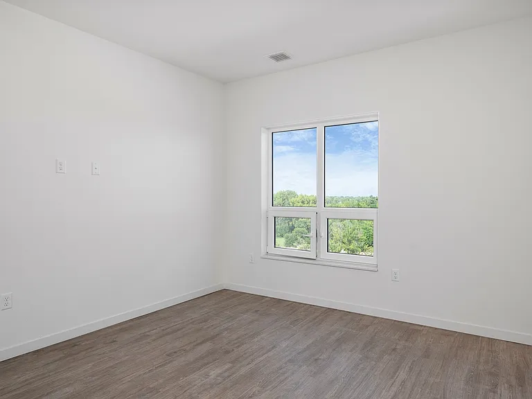 Bright and airy room with modern wooden flooring and a large window offering lush green views. Bright and airy room with modern wooden flooring and a large window offering lush green views.