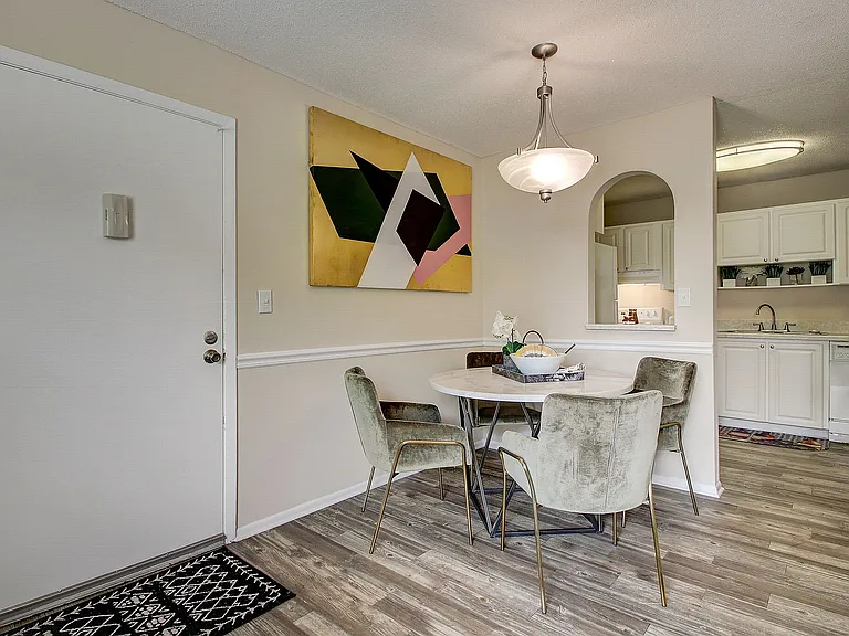 Charming dining area with a modern design, featuring a round table, elegant chairs, and artistic wall decor, seamlessly connected to a sleek kitchen with stylish cabinetry.