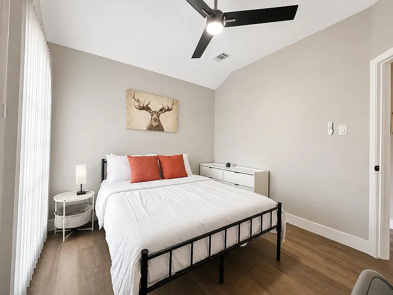 Comfortable bedroom with a full bed, ceiling fan, dresser storage, and large window for natural light.