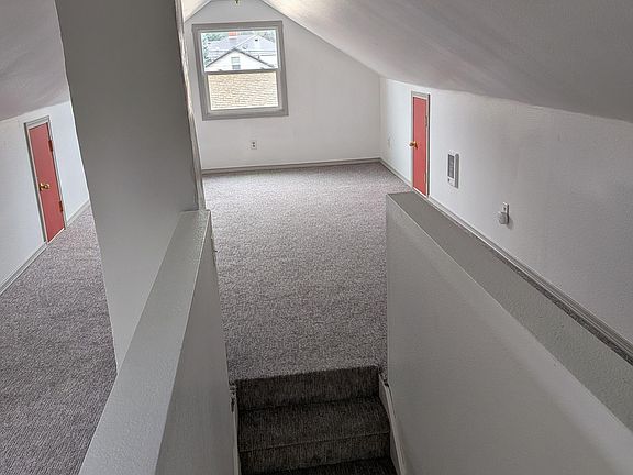 Carpeted upper-level landing with sloped ceilings, overhead lighting, and a window bringing in natural light.