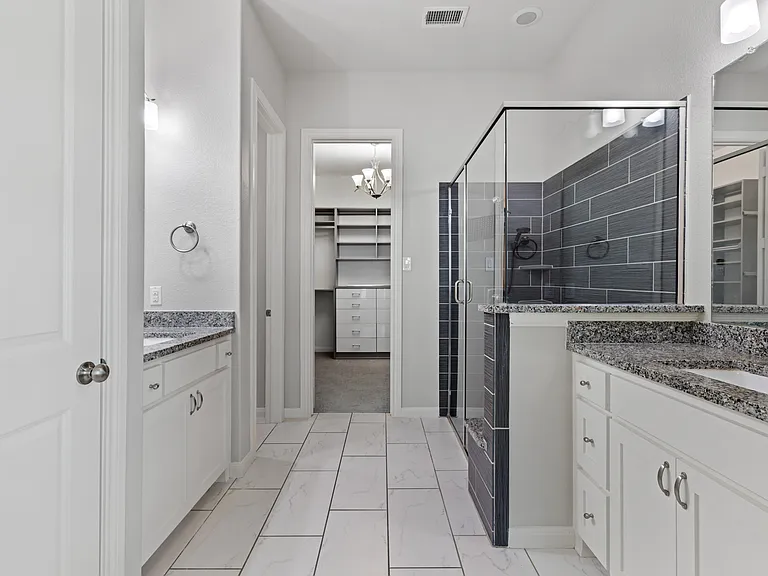 Spa-inspired ensuite bath featuring dual granite vanities, a framed walk-in shower with bench seating and custom walk in closet